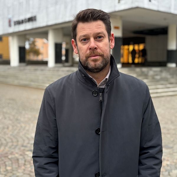 Man i mörk jacka står utanför en byggnad på en stenlagd gård