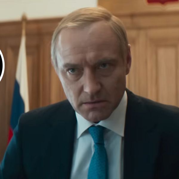 Jude Law som Putin i kostym framför en rysk flagga och träpanel i bakgrunden.