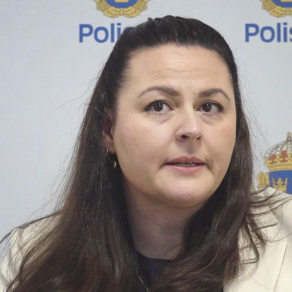 Kvinna sitter framför en vägg med svenska polisens logga.