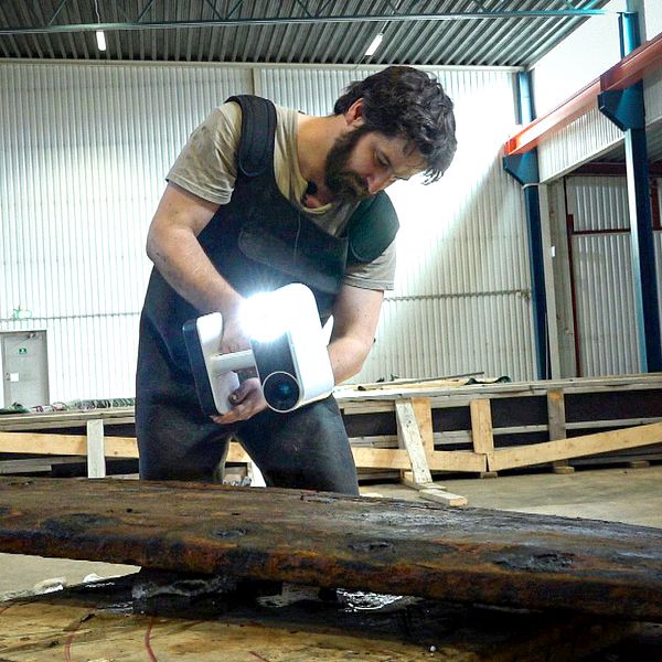 En man står med en skanner över en planka, som tillhör ett skeppsvrak från 1300-talet.