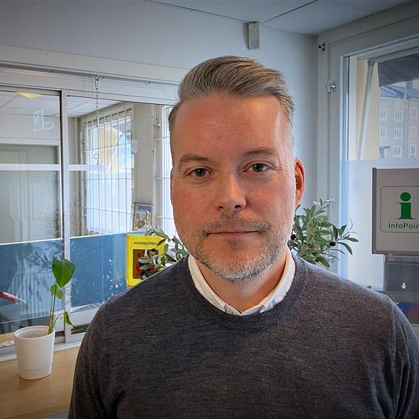 Jonas Eriksson syns en receptionsdisk med några plantor och kontorsmaterial samt en glasvägg med en öppen dörr i bakgrunden.