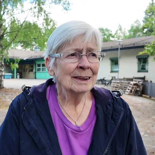 Kvinna med grått hår och glasögon står framför en hälsocentral.