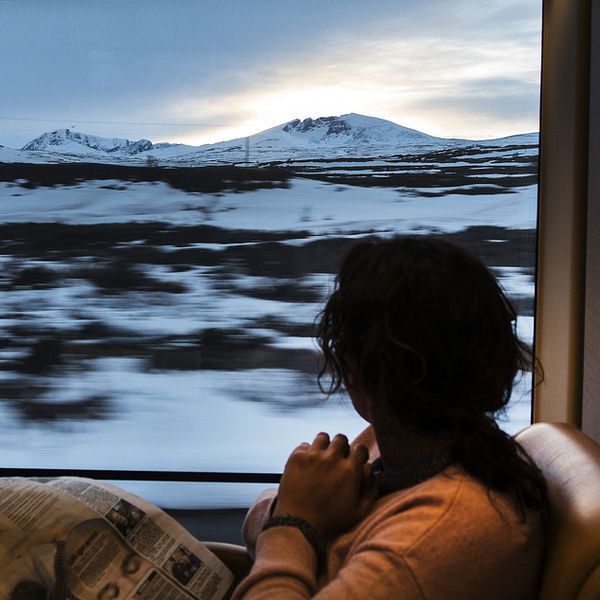 Bild på en kvinna som sitter på ett tåg och läser tidningen.