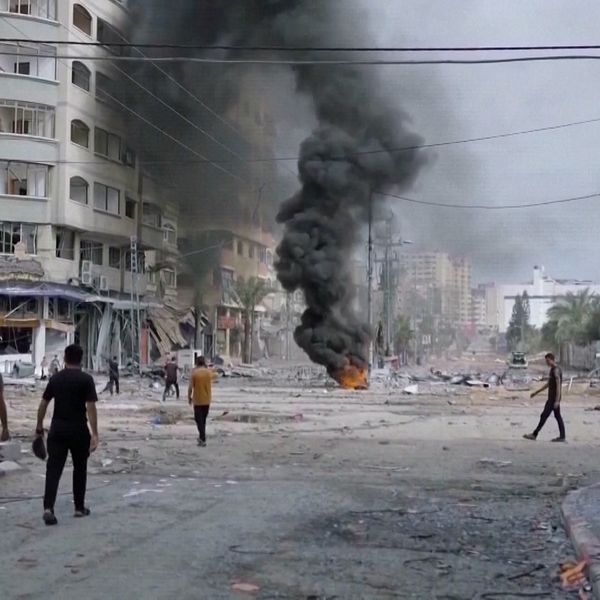 Människor går på gata i Gaza där eld och rök syns.