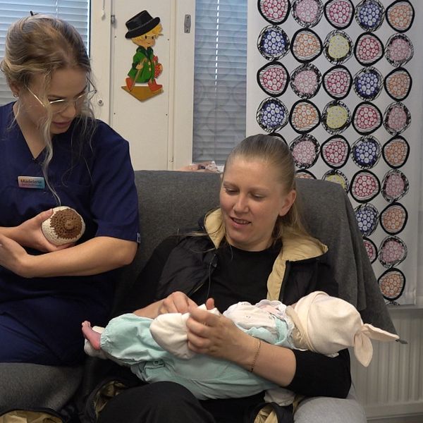 mamma håller i sin bebis, barnmorska sitter bredvid och instruerar om amning