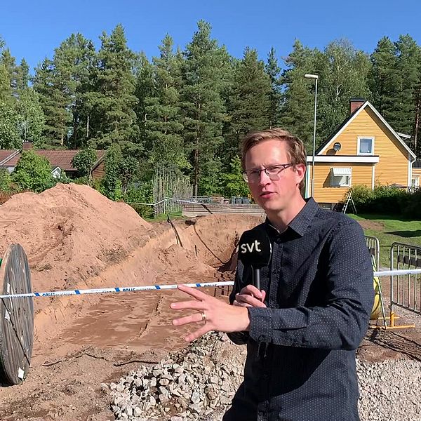 En man med mikorfon står framför en grop som är avspärrad av polisen