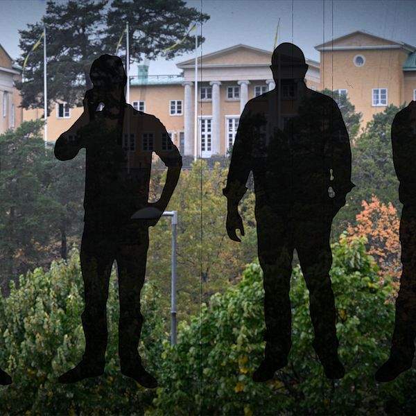 Skolbyggnad i bakgrunden med fyra mörka silhuetter i förgrunden