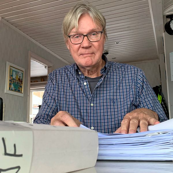 Gunnar Holmberg sitter vid köksbordet. Framför sig har han en pärm full med viktiga dokument.