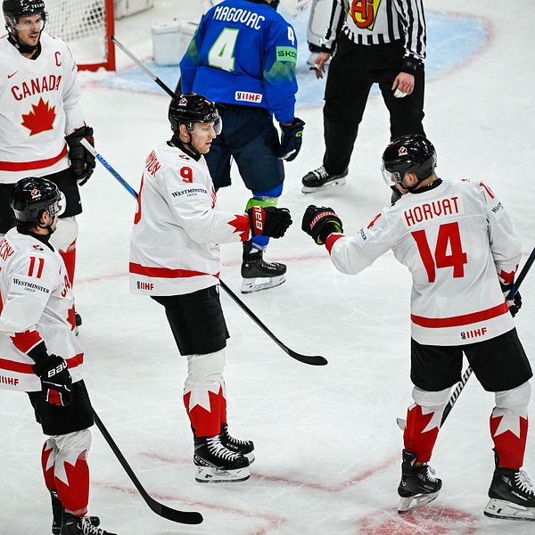 Fyra kanadensiska ishockeyspelare firar på isen under match mot blåklädda motståndare.