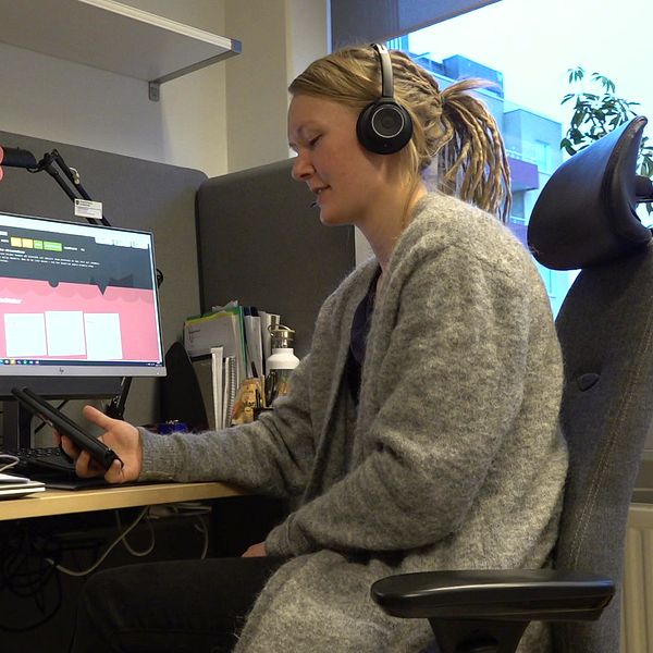 kvinna med hörlurar framför dator tittar på mobiltelefon