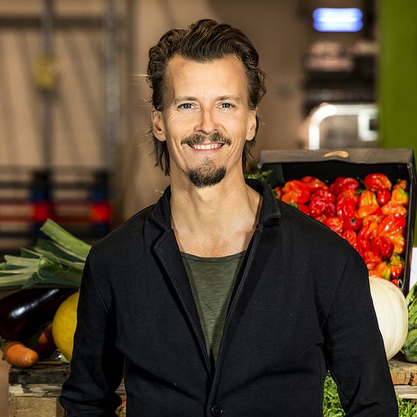 Paul Svensson står iklädd grön t-tröja och mörk kavaj. Bakom honom skymtas grönsaker i ett kök.