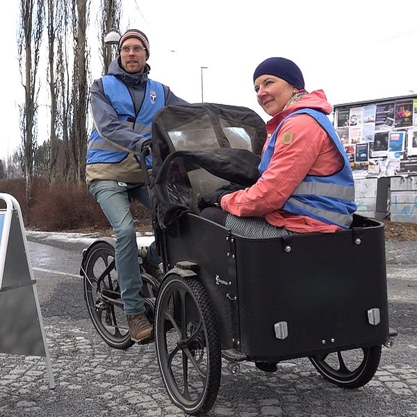 Två personer på lådcykel vid skylt som tackar för att man går eller cyklar.