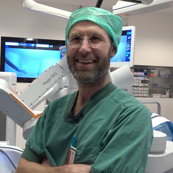 Överläkaren Mattias Tell står leende i gröna operationskläder framför en maskin – en operationsrobot