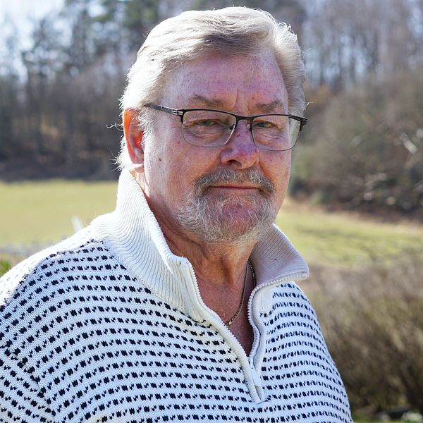 Prostatacancersjuka Keith Olsson med vit tröja står utomhus en solig vårdag. han berättar vad han tänker om att alla cancerspecialister slutat i Blekinge.