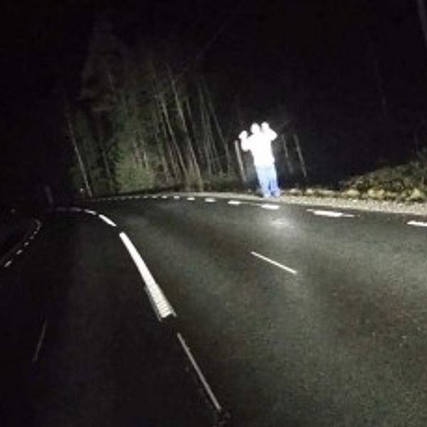 Mörk landsväg nattetid med två personer synliga i vägbanan i strålkastarljus