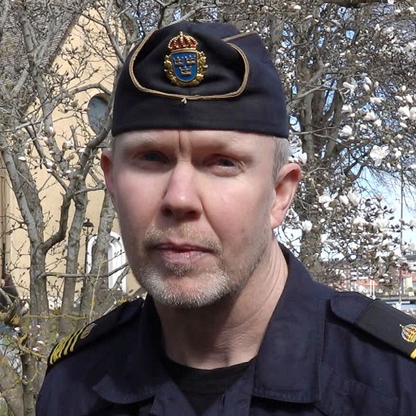 Polisman står framför ett träd vid en byggnad.
