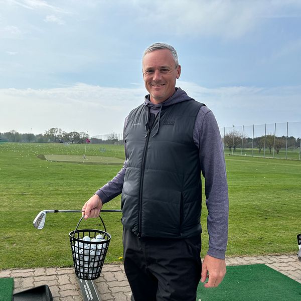 En person står på en golfbana och håller en korg med golfbollar.