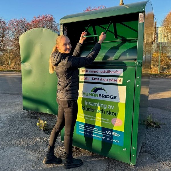 en kvinna, avfallsstrateg som slänger kläder i en sopcontainer (klädcontainer) som är grön.
