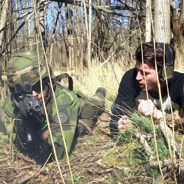 Kamouflerad soldat ligger i buskage under övning i skogen.