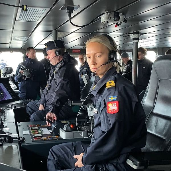 Besättningsmedlemmar i uniformer arbetar i kommandobryggan på ett fartyg, omgivna av avancerad navigationsutrustning och olika kontroller.