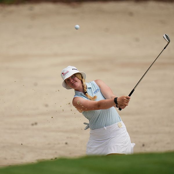 Golfspelare slår upp bollen ur en sandbunker mot greenen.