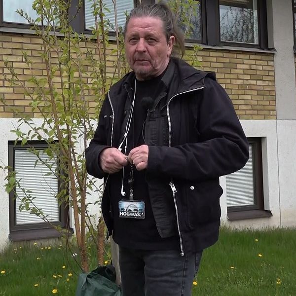 Person med ID-bricka står utomhus framför en byggnad med gula tegelväggar och fönster.
