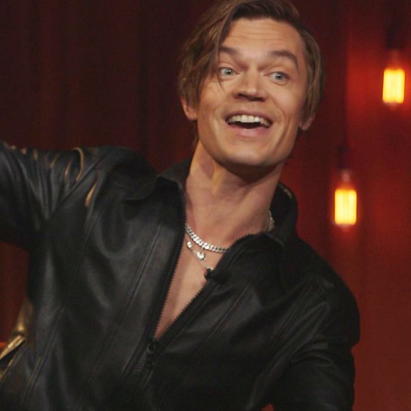 Person i svart skinnjacka i tv-studio med hängande lampor och röd bakgrund.