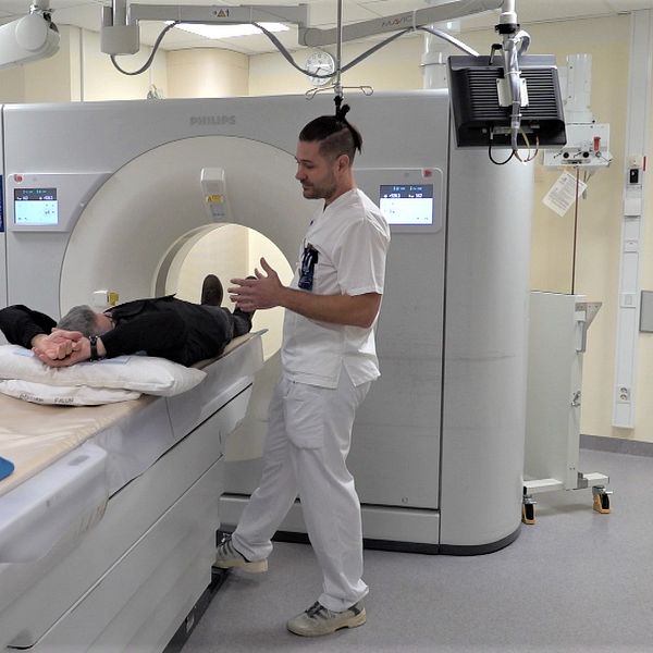röntgensjuksköterskan Henrik Paulfors vid en röntgenmaskin och en person på väg in i tunneln i apparaten..