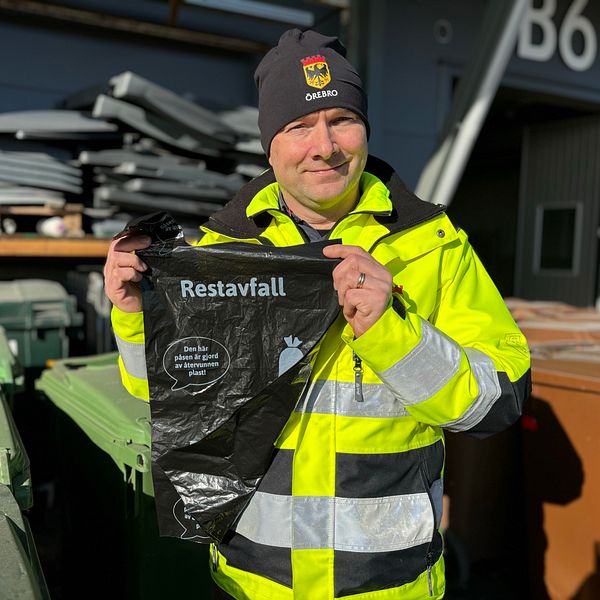 Ola Eklöf i varselkläder håller en svart soppåse märkt ”Restavfall” vid Örebro kommuns återvinningscentral.