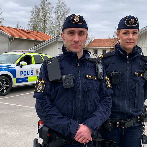 En manlig och en kvinnlig polis står framför sin polisbil