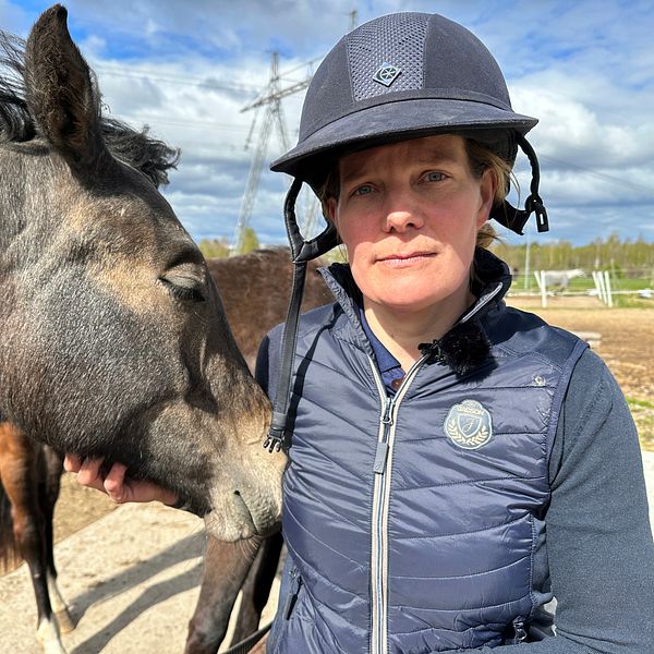 En person med ridhjälm står nära en häst som nosar mot personens axel utomhus.