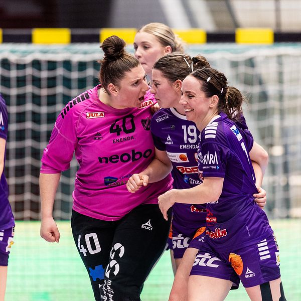 Fyra handbollsspelare samlas vid målet under en match i en inomhushall.