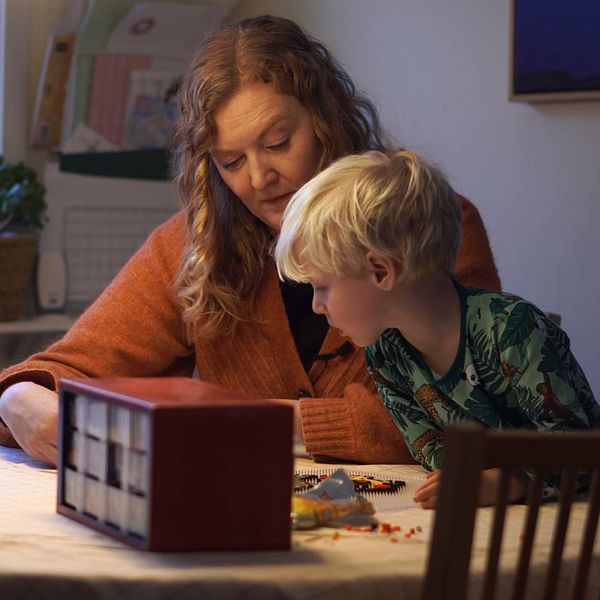 En mamma och ett barn sitter vid ett bord och lägger pärlplattor