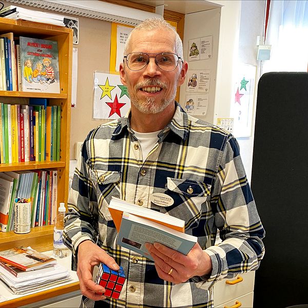 Jörgen Hellman, specialpedagog, står med en rubits kub och några böcker i handen. Bakom är en bokhylla.