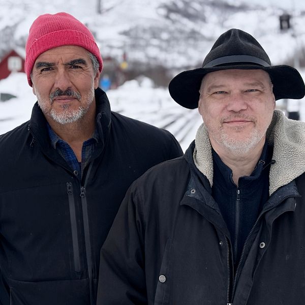 Rafael Edholm och Björn Olofsson, författare till romanen Svarta Björn, står bredvid varandra vid snötäckta järnvägsspår och röda hus.