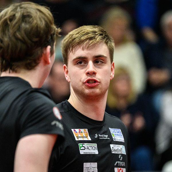 Två bordtennisspelare i svarta tröjor samtalar under en match inför publik.