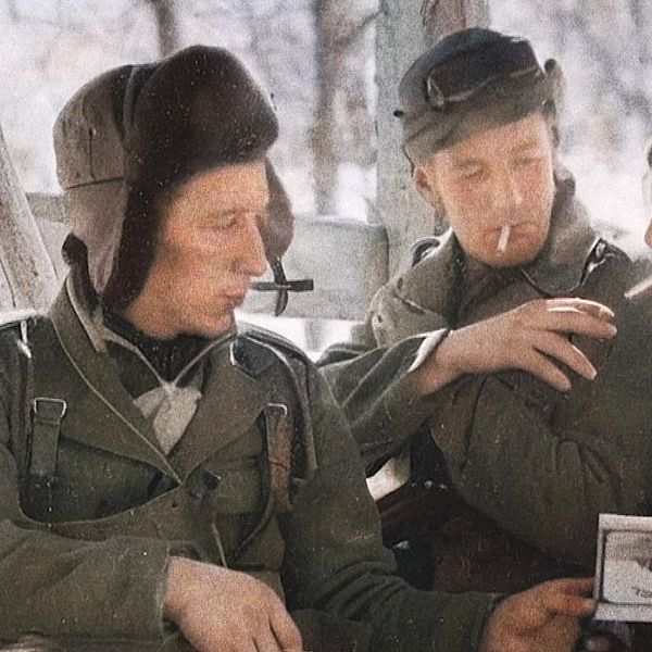 Fyra personer i soldatuniform samtalar och röker cigaretter utomhus.