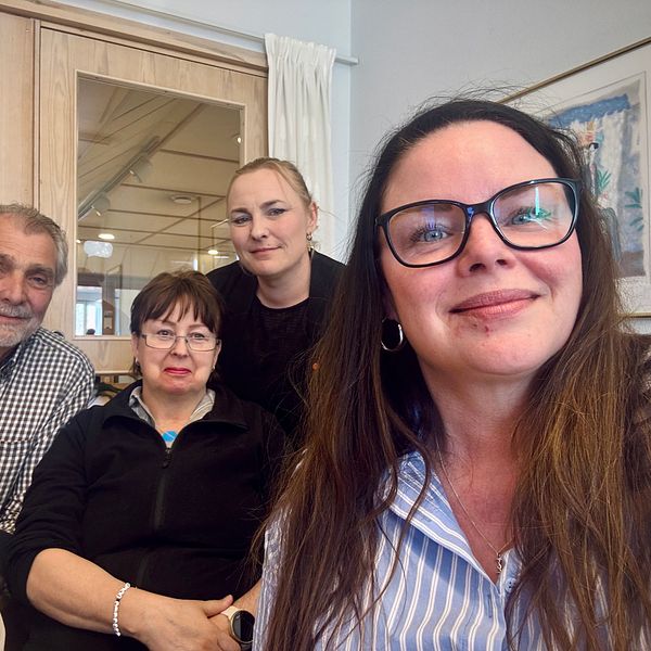 Fem personer sitter tillsammans inomhus framför ett fönster och en tavla.