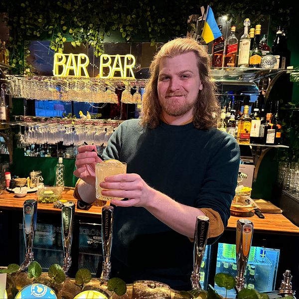 Bartender serverar en drink i en livlig bar med flaskor och glas i bakgrunden.
