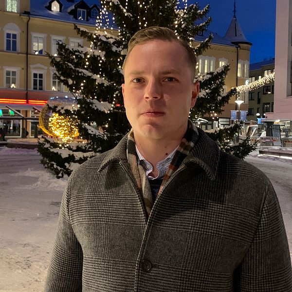 Det socialdemokratiska regionråd i Region Dalarna, Sebastian Karlberg, står utomhus framför en stor julgran.