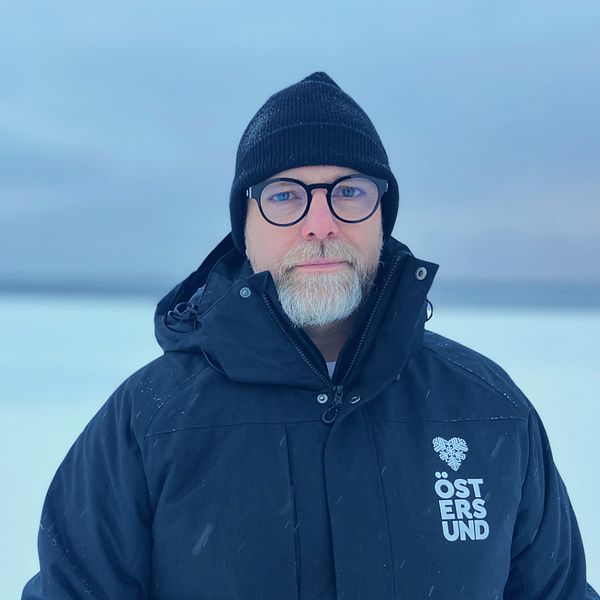Anders Wennerberg, kommundirektör i Östersund står i mörk hacka, mössa och glasögon framför en frusen Storsjön.