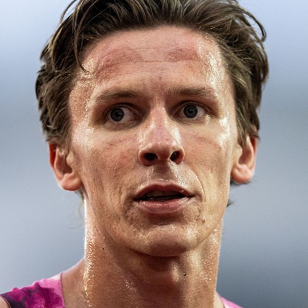 En man i en rosa tävlingsdräkt strax efter en idrottstävling. Hans hår är mörkt och bakgrunden är suddig, vilket antyder att han befinner sig utomhus.