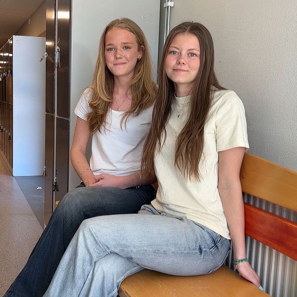 Två unga kvinnor sitter på en bänk i en korridor