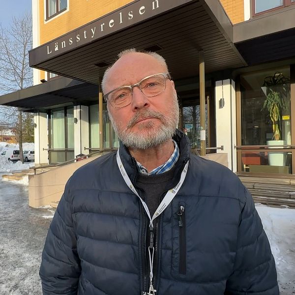 En person står framför ett Länsstyrelsen-kontor i ett vinterlandskap med snö på marken och träd i bakgrunden.