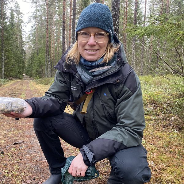 På bilden är Linda Andersson, rovdjurshandläggare på Länsstyrelsen. Hon sitter på huk på en skogsväg, i handen håller hon en plastpåse.