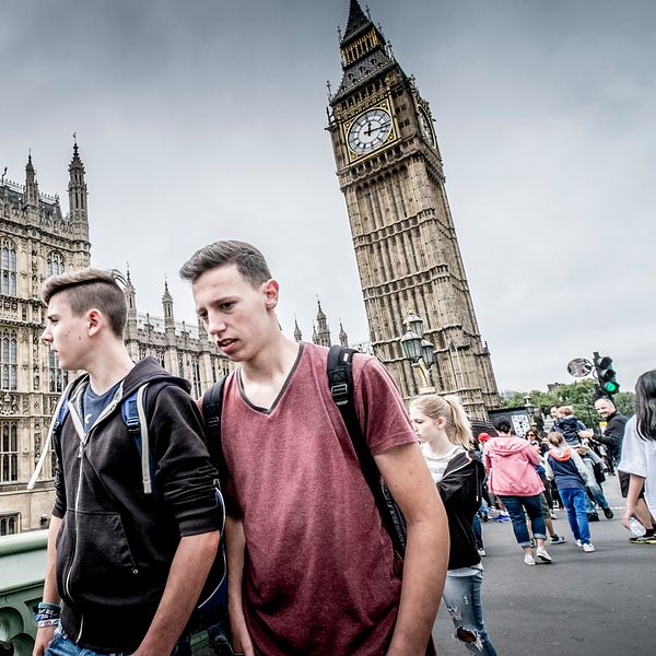 Ung man står framför Big Ben i London. Folk går på bron i bakgrunden.
