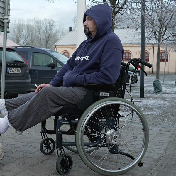Jevhen Kovalenko sitter i rullstol utomhus i Sverige, klädd i hoodie och sandaler.