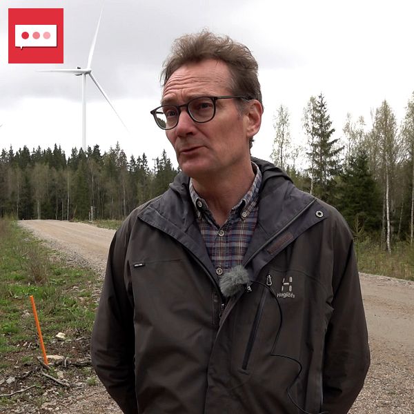 Man på landsväg i skog, med vindkraftverk synligt i bakgrunden.