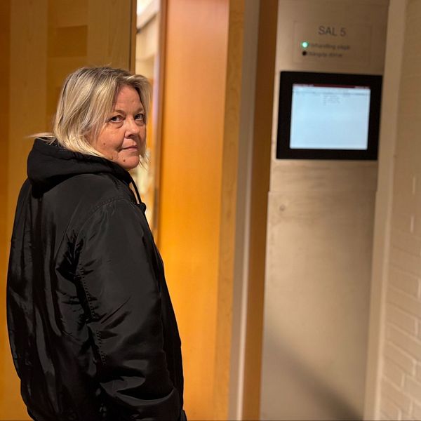 Person stårframför ett rum med en halvöppen dörr synlig i bakgrunden.