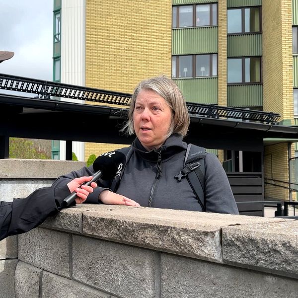 Reporter intervjuar en person vid en mur utanför ett flerbostadshus.